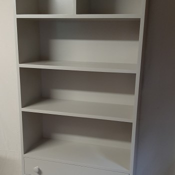 A stand-alone storage unit for a baby room, painted in light grey.